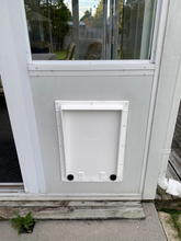 A white pet door installed in a wall below a window.