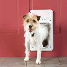 A dog is halfway through a white dog door installed in a red door.