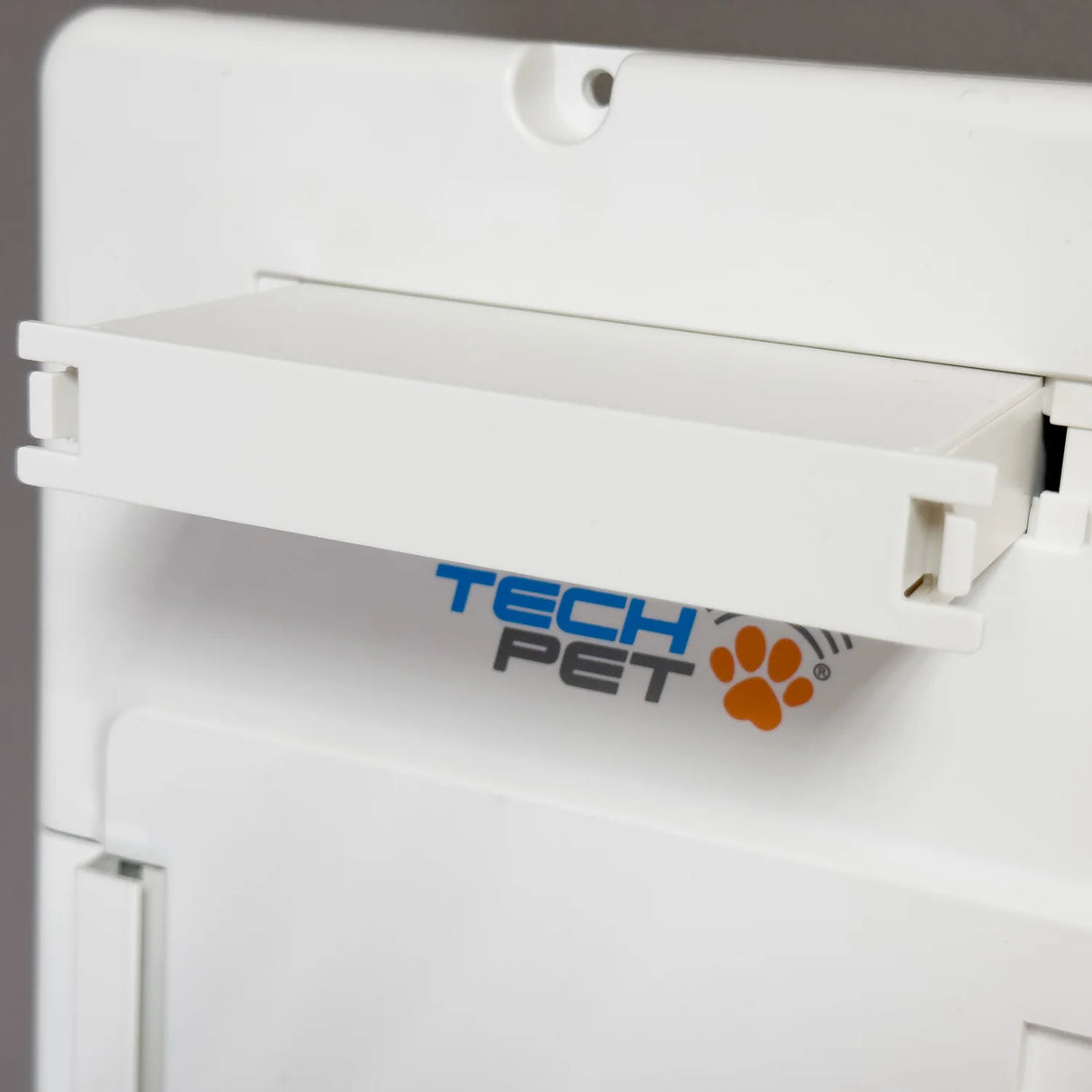 High Tech rechargeable battery for Roll Up power pet doors, a white rectangular plastic housing with a brass connector slot on the lower edge, photographed at a three-quarter overhead angle on a dark wooden surface.