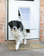 A black and white dog is walking through a dog door onto a doormat that reads