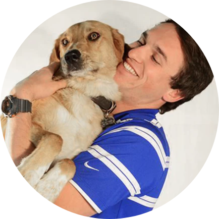 A smiling man in a blue striped shirt hugs a tan-colored dog.
