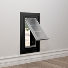 A pet door is installed in a white wall with wood flooring.