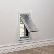 A pet door with a flexible flap is installed in a white wall.