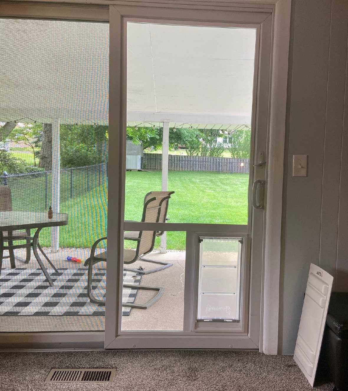Interior view of a sliding glass door with a pet door insert, looking out to a patio and yard.
