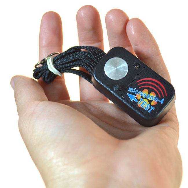 A hand holds a black "microsonic-4 TEST" device with a lanyard.