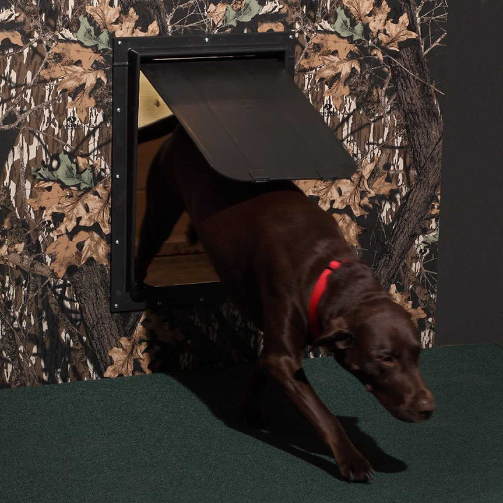 A brown dog with a red collar exits a camouflage-patterned wall through a black dog door.