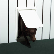 A brown dog walks through a white dog door in a white fence.