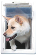 A light-colored dog is going through a white plastic pet door with a clear flap.