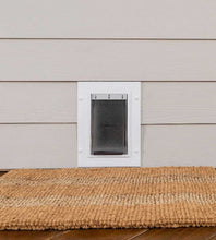 A pet door is installed in light siding above a natural fiber mat.