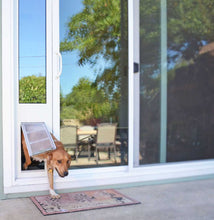 A dog going through a dog door in a sliding glass door.