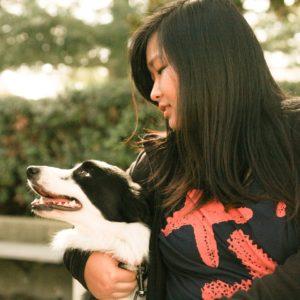 A woman affectionately holding a happy black and white Border Collie to her side. 