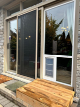 Patio door with a pet door in a fixed glass panel and a wooden step outside.