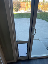 A sliding glass door with a pet door insert leads to a concrete patio and grassy backyard.