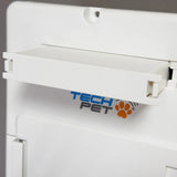 High Tech rechargeable battery for Roll Up power pet doors, a white rectangular plastic housing with a brass connector slot on the lower edge, photographed at a three-quarter overhead angle on a dark wooden surface.