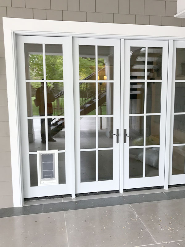 A multi-paneled glass door with a dog door installed in the bottom left panel is shown from the outside.