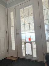 A white glass paneled door with a dog door insert is viewed from inside.