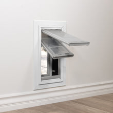 A pet door with two open flaps is installed in a white wall above a baseboard.