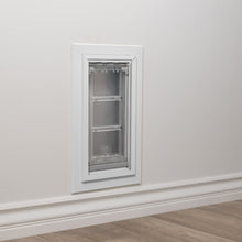 A pet door installed in a white wall, with a white baseboard and wood-look flooring visible.