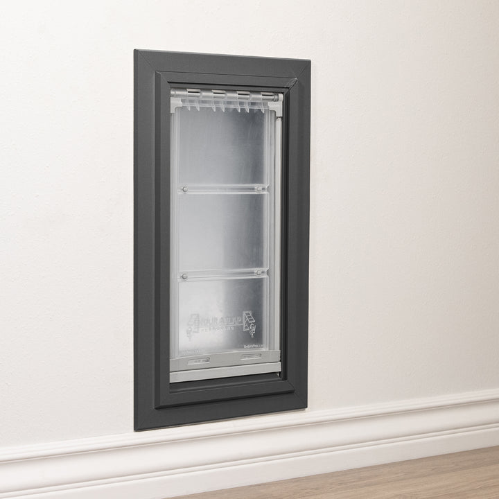 A pet door with a gray frame is installed in a white wall.