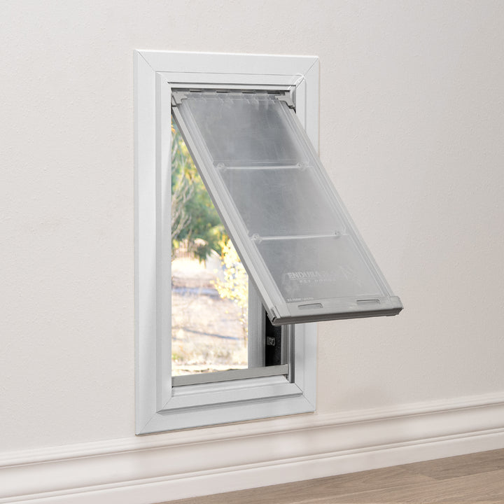 A pet door is installed in a white wall, with the clear flap partially open.