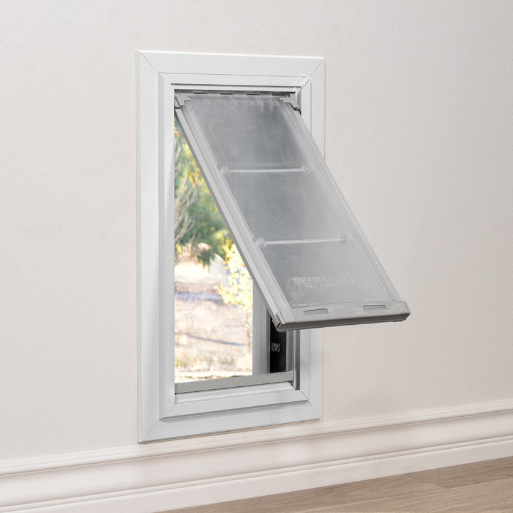 A white-framed pet door is installed in a wall, with the flap partially open, revealing a view of the outdoors.