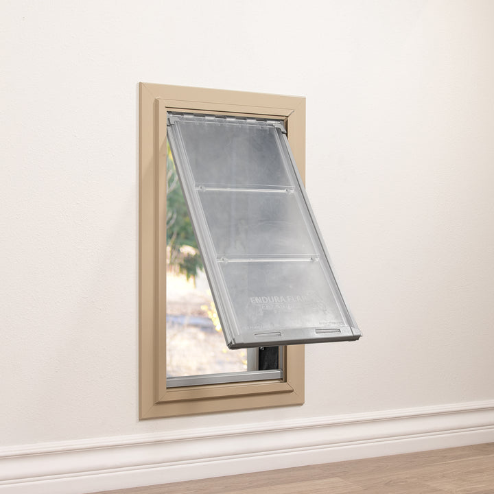 A beige-framed pet door, labeled "Endura Flap," is installed in a wall with a partial view to the outdoors.