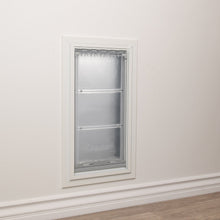 A pet door with a clear, hinged flap is installed in a white wall.