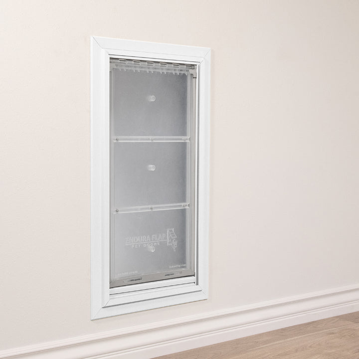 A white-framed "Endura Flap" pet door is installed in a beige wall above white trim.