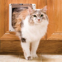 A long-haired cat is emerging from a pet door in a wooden door.