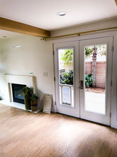 Interior view of a room with light-colored wood floors, a fireplace, and double doors with a dog door insert.
