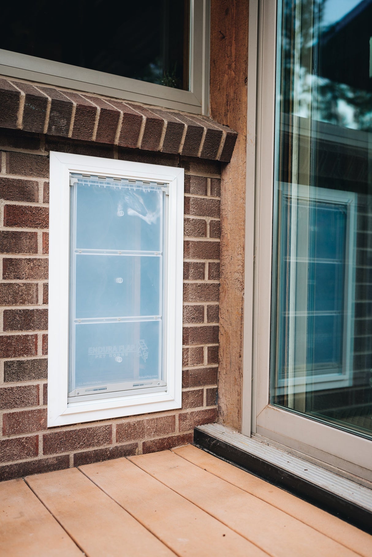 A pet door is installed in a brick wall next to a glass sliding door.