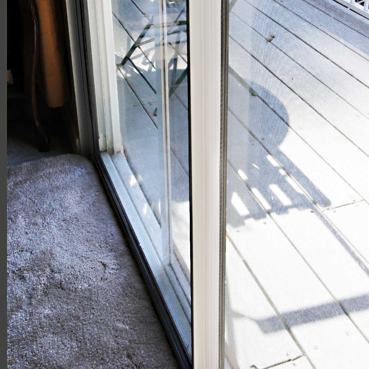 View through a sliding glass door onto a deck with a gray carpet inside.