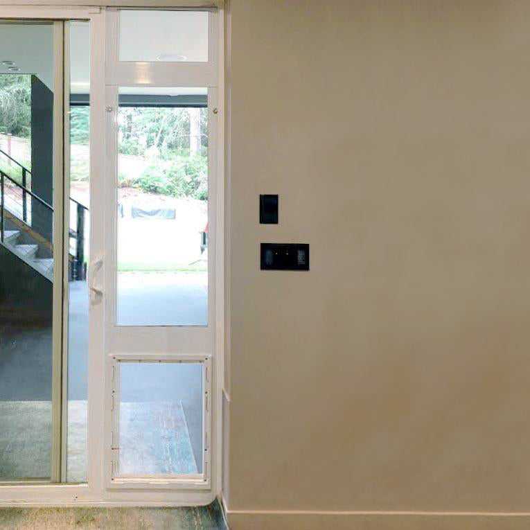 Interior view of a sliding glass door with a built-in dog door panel, next to a beige wall with black electrical outlets.
