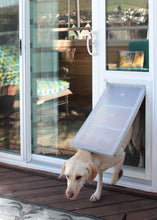 A golden Labrador Retriever exits a white sliding glass door with a dog door insert onto a wooden deck.